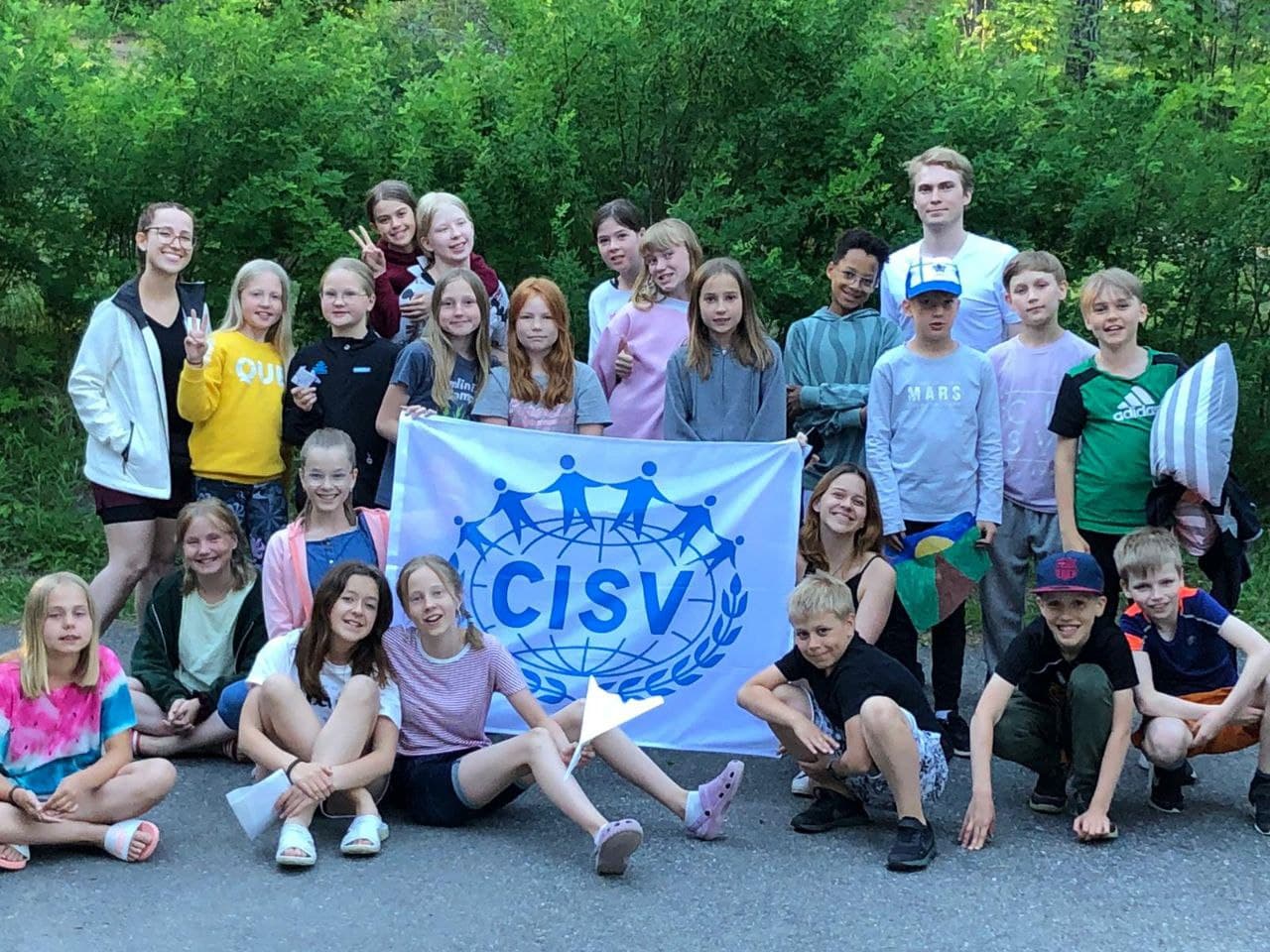 Group of people smiling and holding a CISV-flag